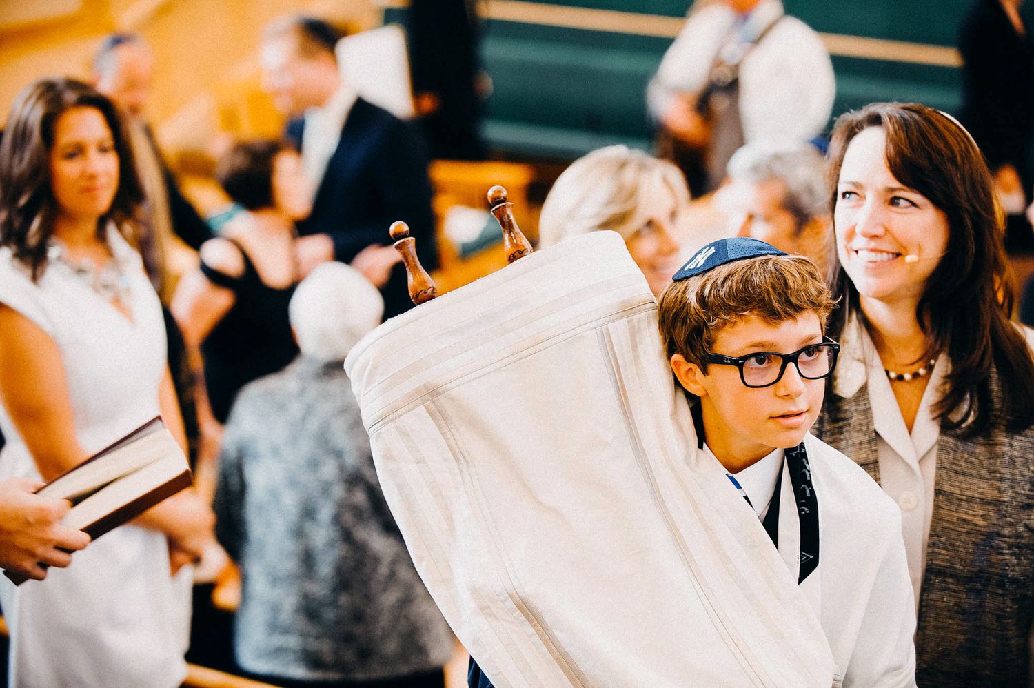 A person in glasses and a tie holds up a white cloth in a room filled with people during an event.