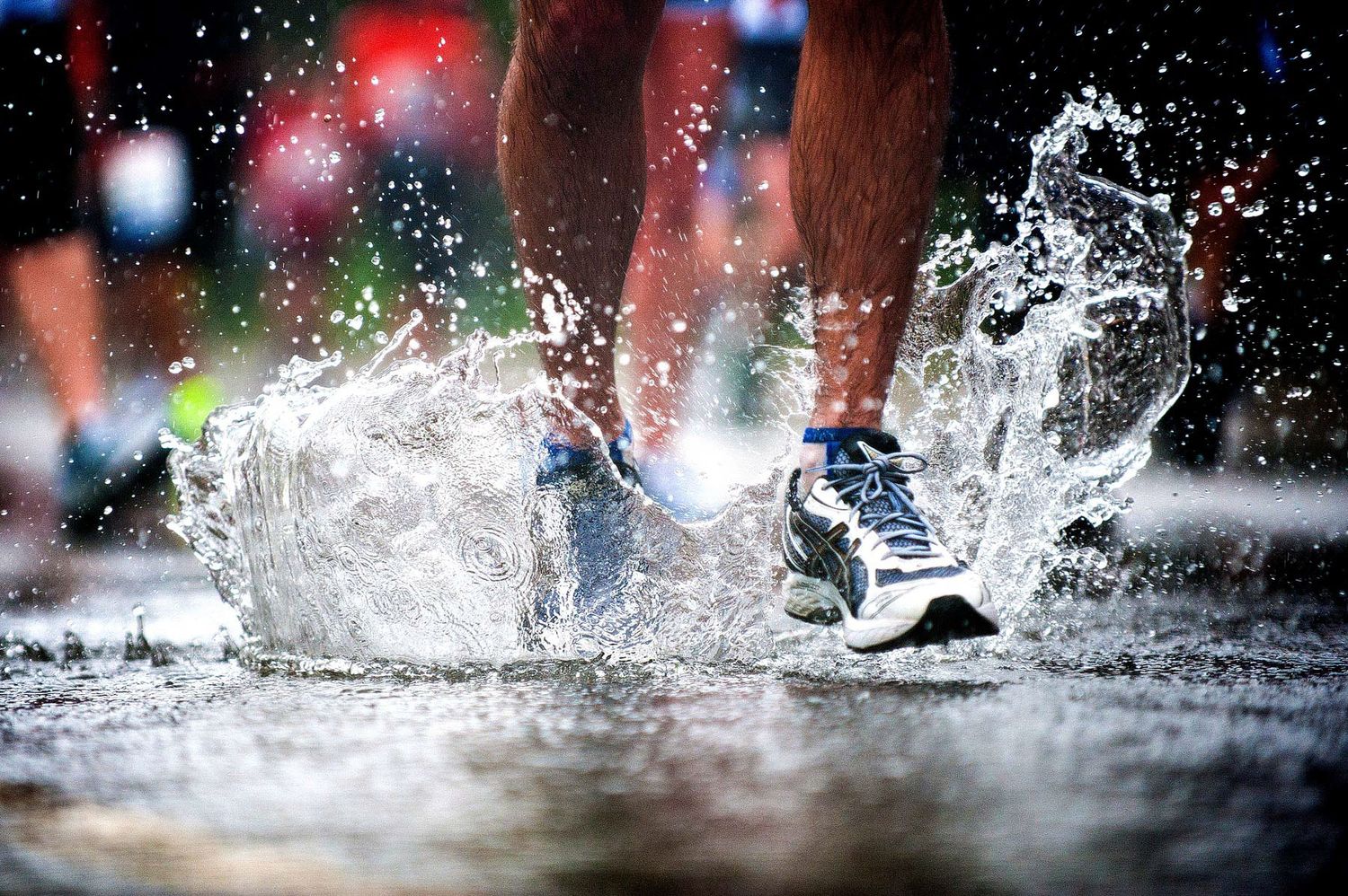 Running shoes splashing through water puddles with colorful lights in the background.