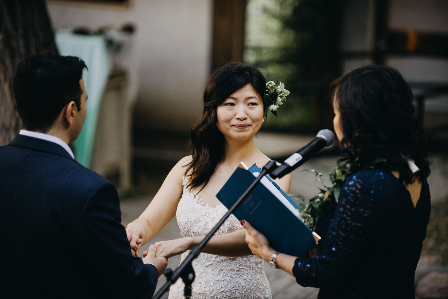 A wedding couple embraces during their outdoor garden ceremony while guests look on in the background.