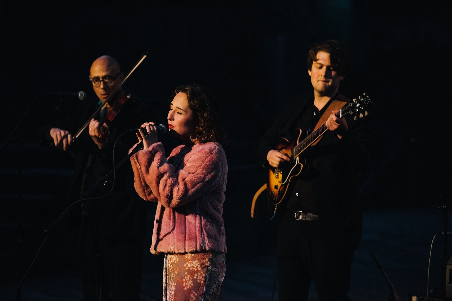 Musicians performing on stage with instruments including violin and guitar during a live concert performance.