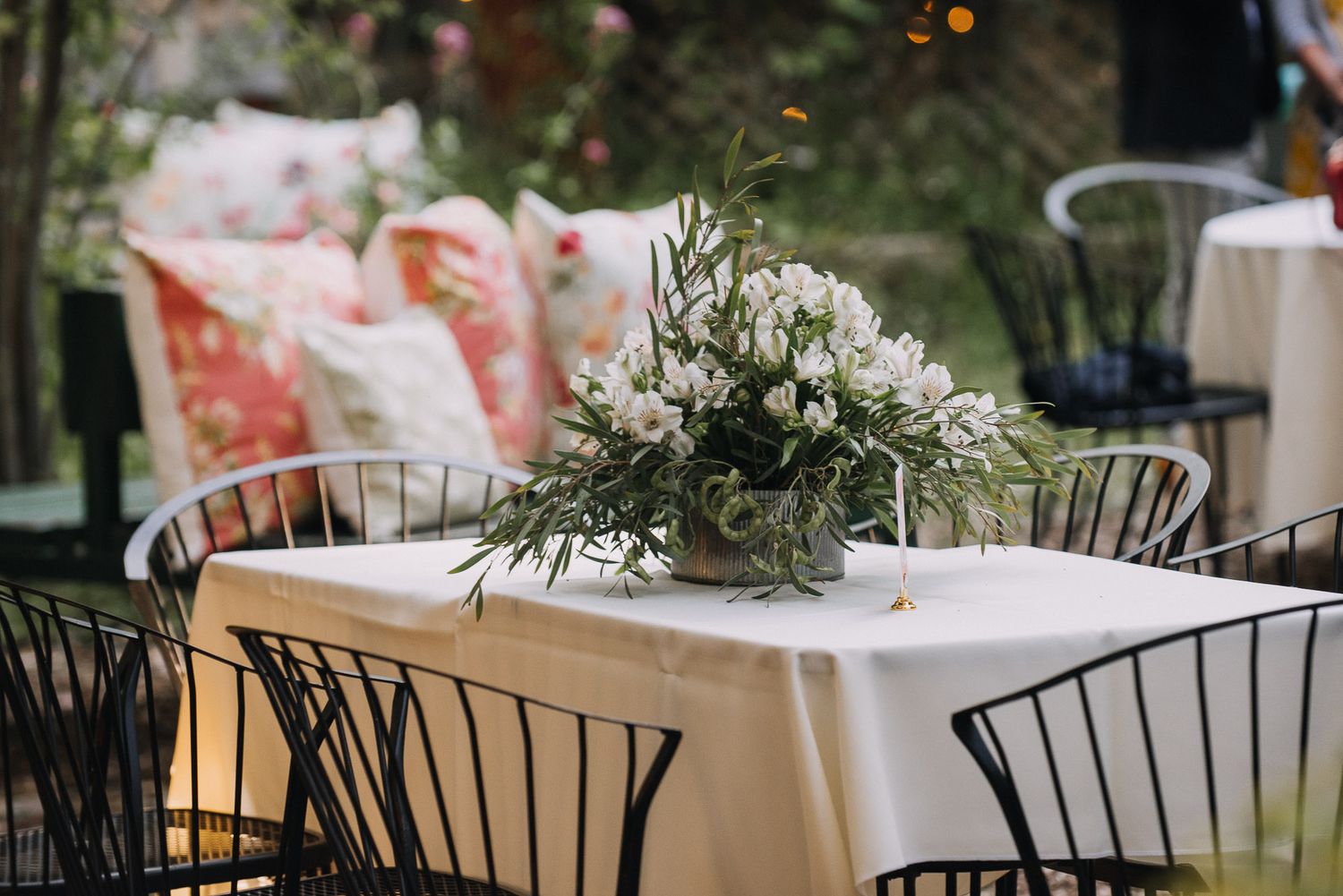 A rustic outdoor wedding reception setup with white tablecloths and black chairs under a tent canopy.