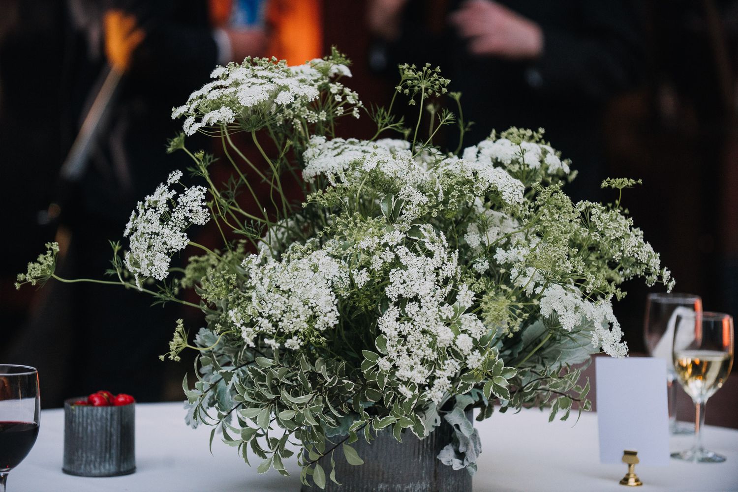 Elegant wedding reception table decorated with white floral arrangements and glassware against a dark background.
