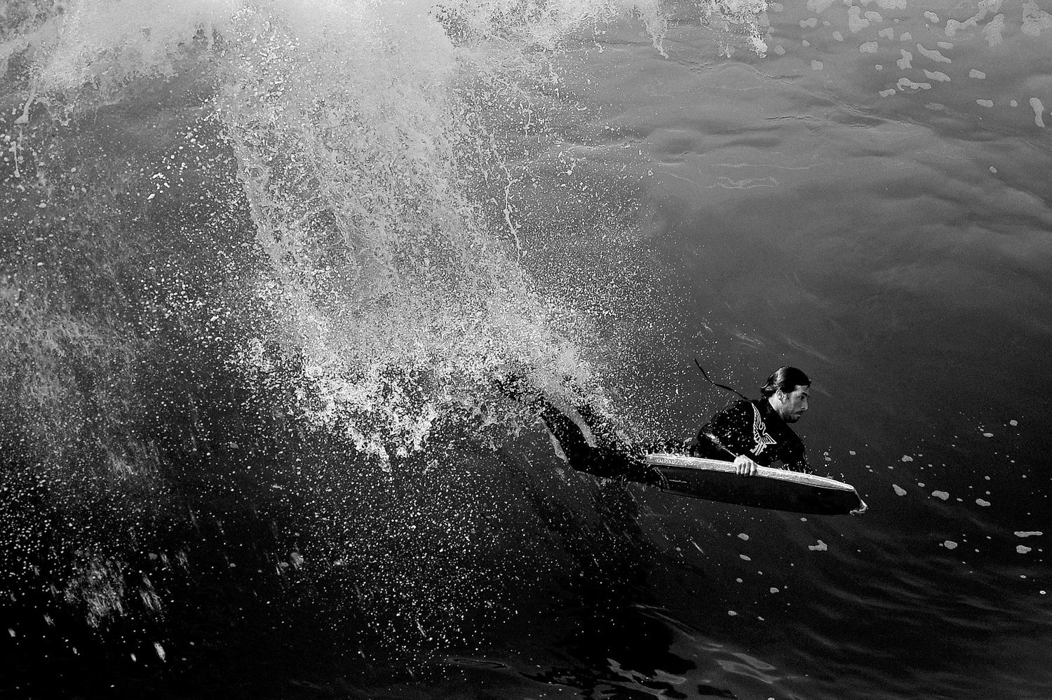 A surfer rides a wave creating dramatic water spray in black and white photography.