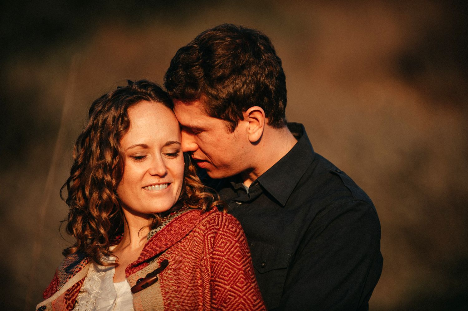 A romantic couple embraces in warm sunset lighting while wearing red and black clothing.