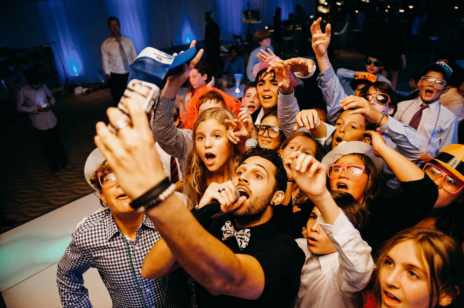 An excited crowd reacts enthusiastically with raised arms and animated expressions during an event.