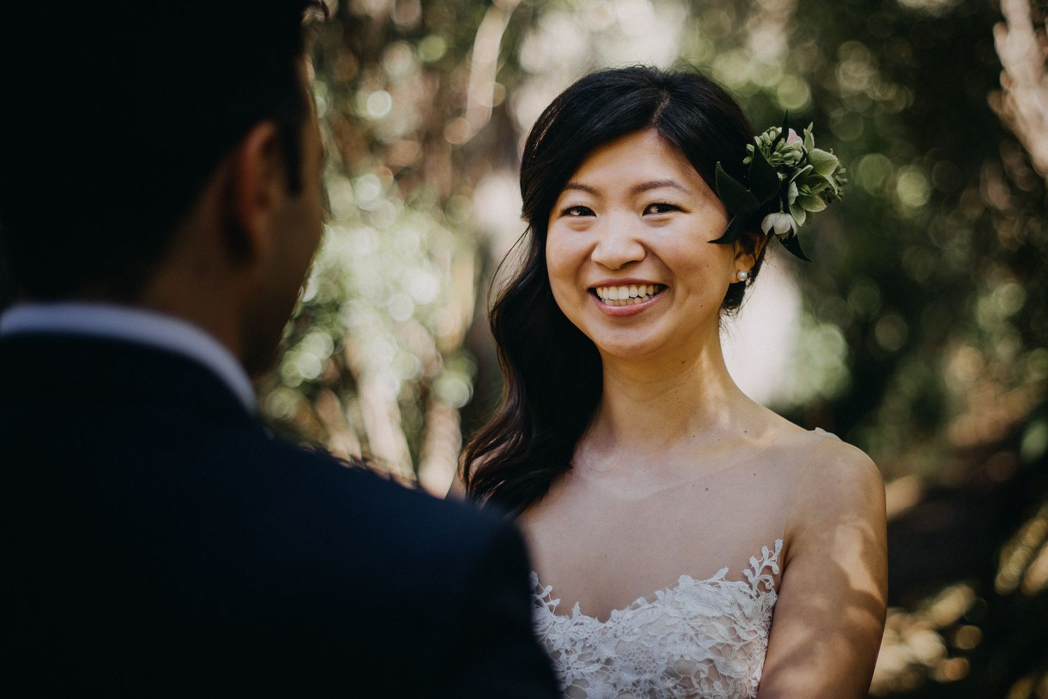A wedding couple shares a romantic moment together in a sun-dappled outdoor garden setting.