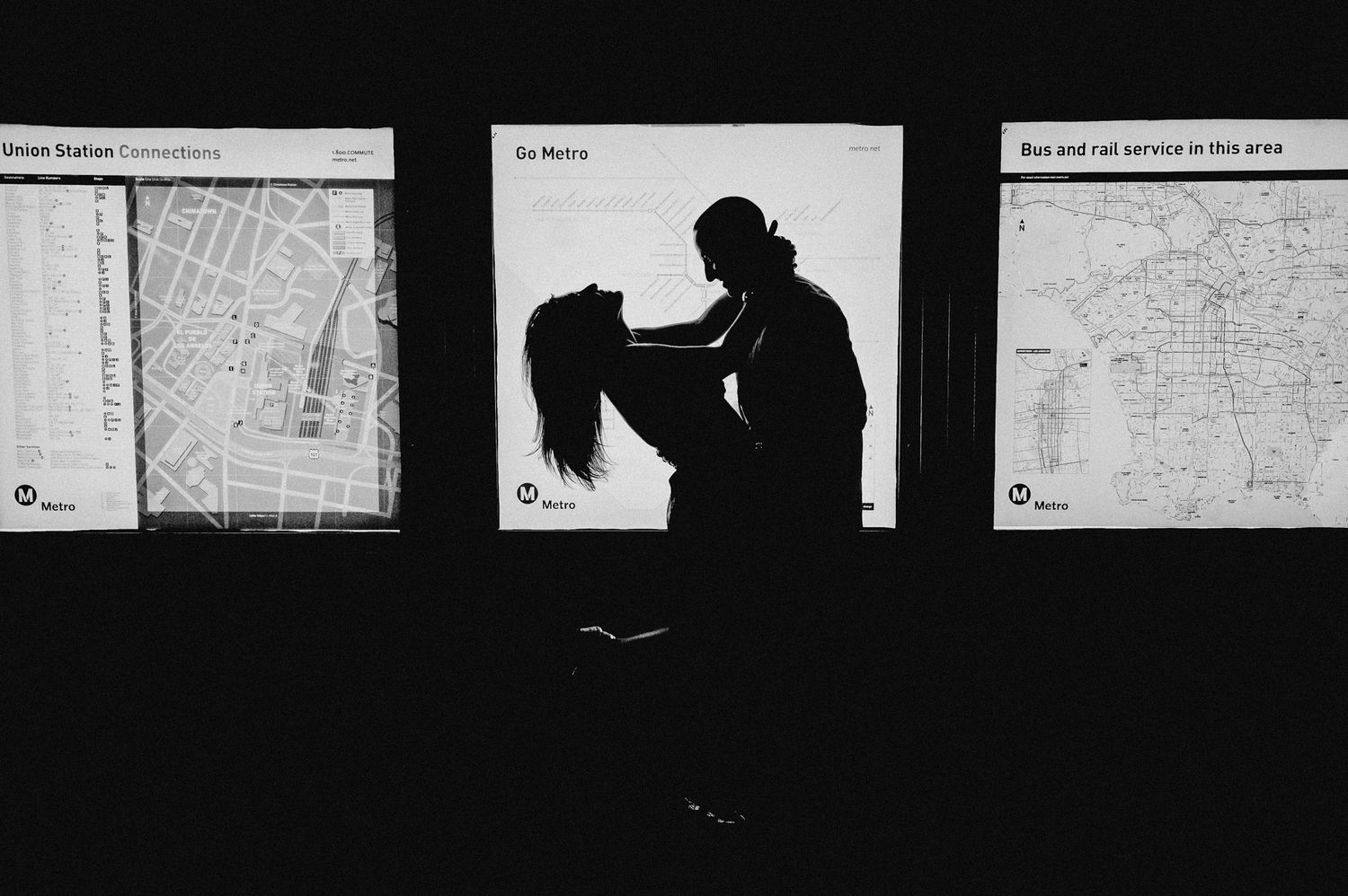 Silhouettes of two people embracing in front of illuminated wall maps.