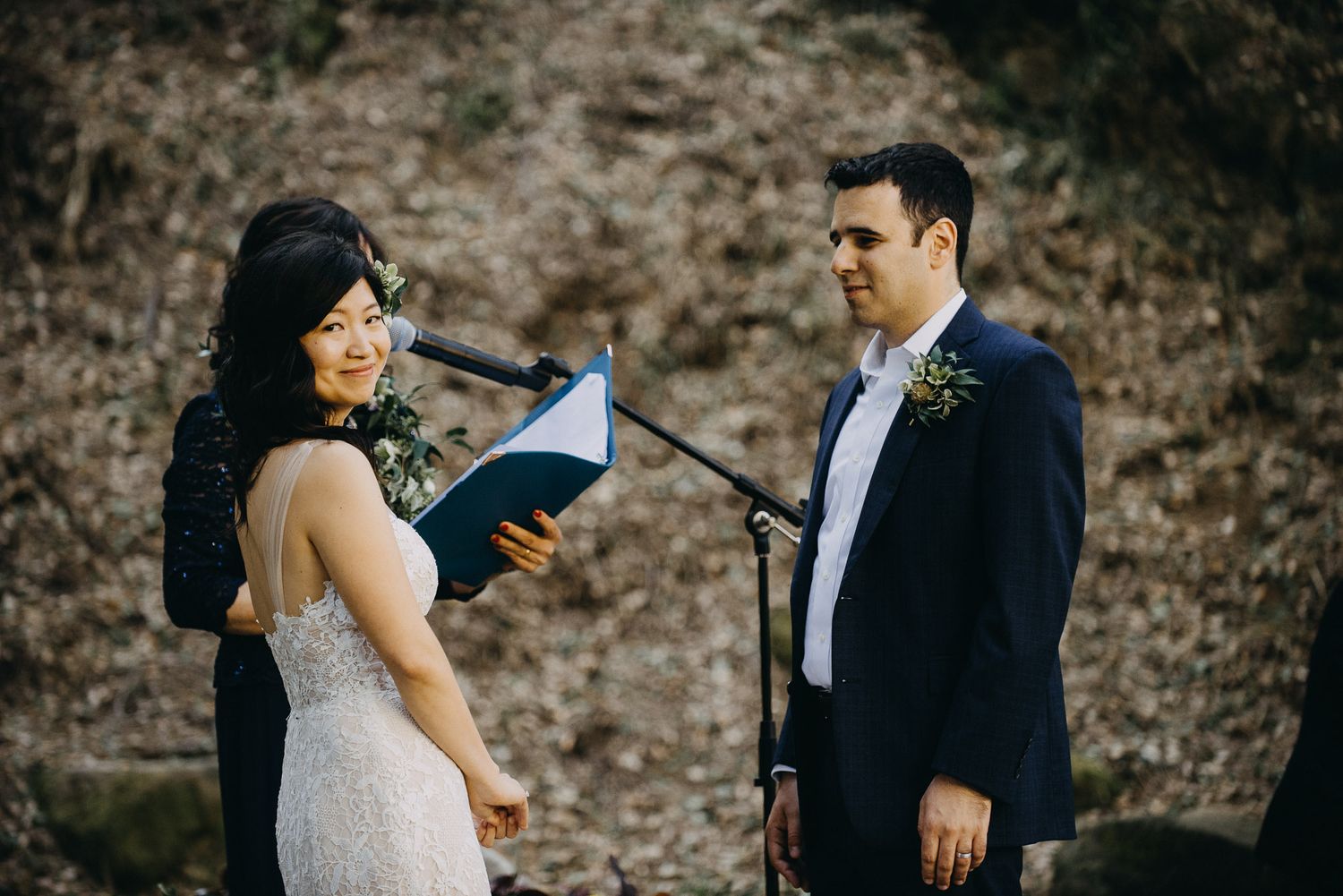 Outdoor wedding ceremony with couple reading personal vows in a wooded natural setting.