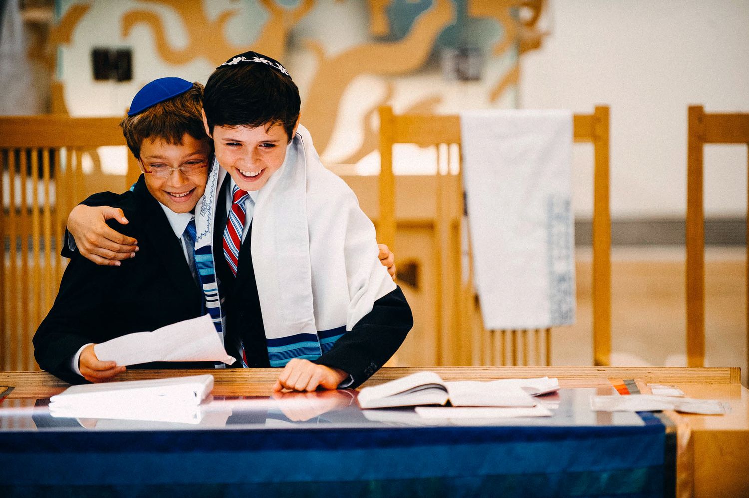 Two students work together at a desk while looking over papers and worksheets in a classroom setting.