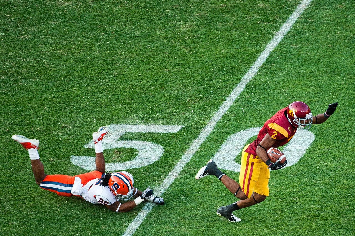 Player in orange evades a tackle attempt on a green football field during a game.