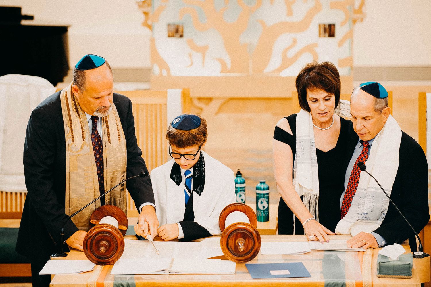 A group gathers around a Torah scroll during a traditional Jewish reading ceremony at a synagogue.
