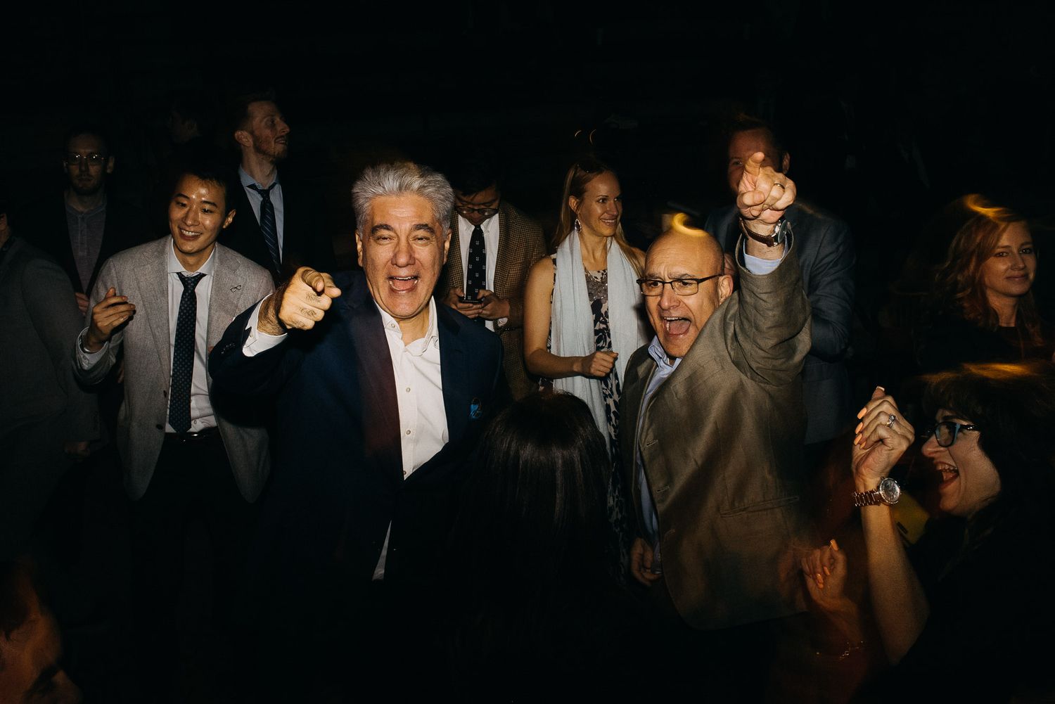 People in formal attire enjoying a social gathering in a dimly lit venue with laughter and conversation.