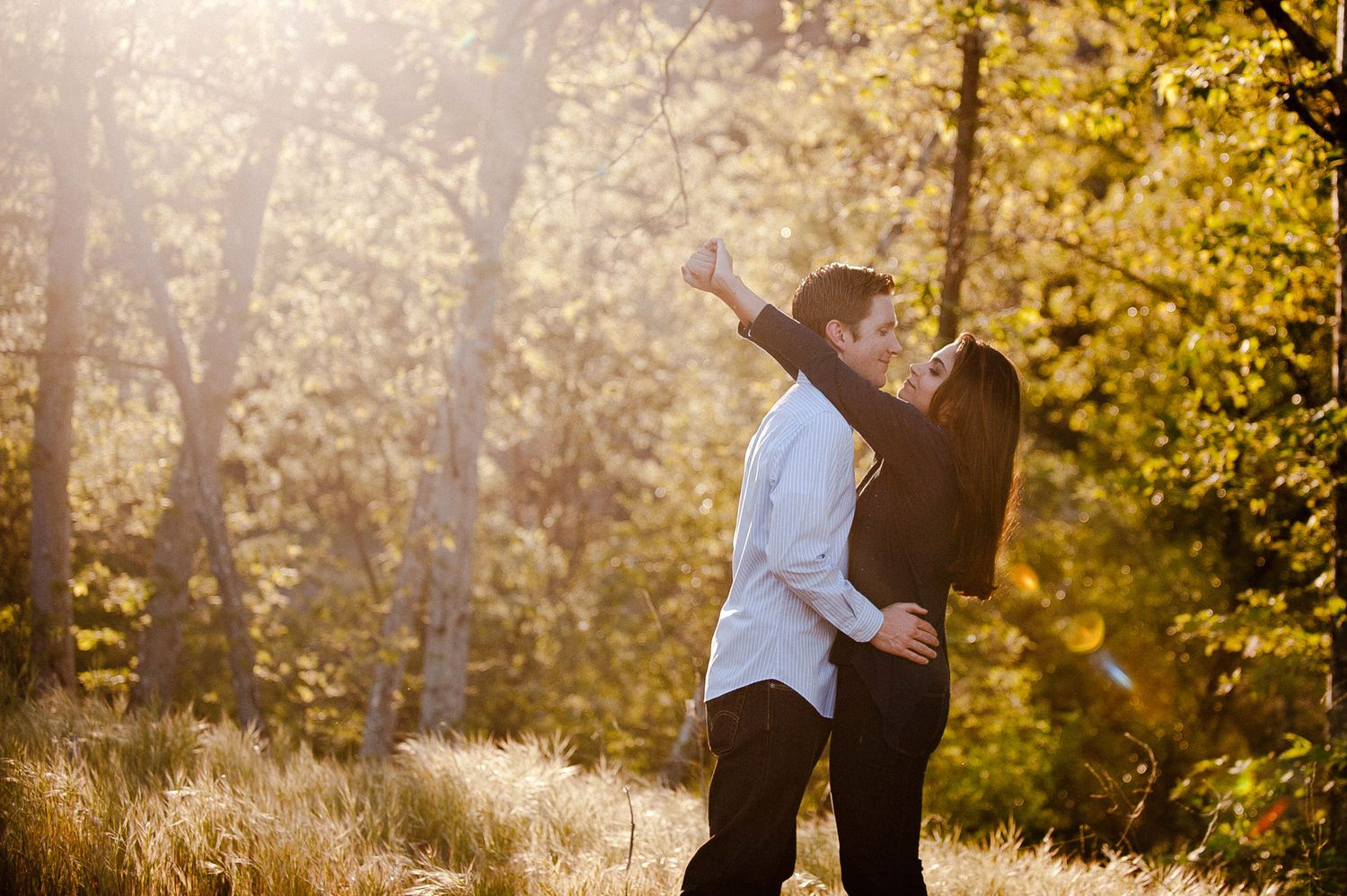 A romantic couple embraces in golden sunlight while surrounded by autumn foliage in a forested setting.