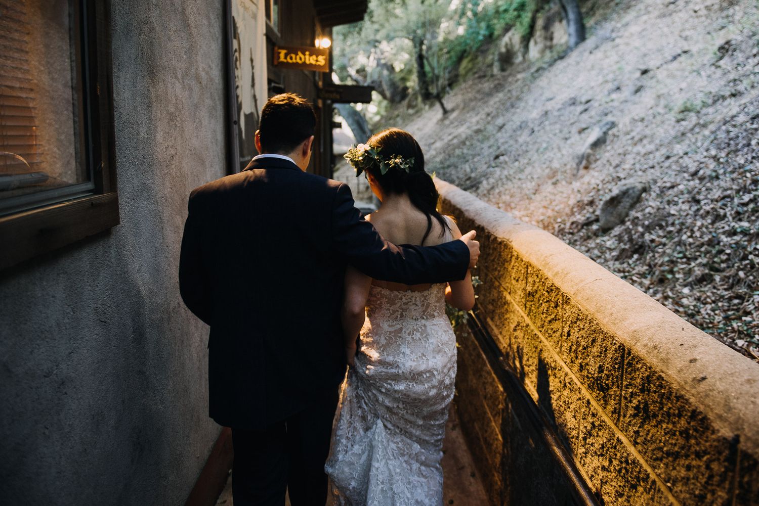A couple walks along a rustic stone pathway illuminated by warm glowing lights during an evening celebration.