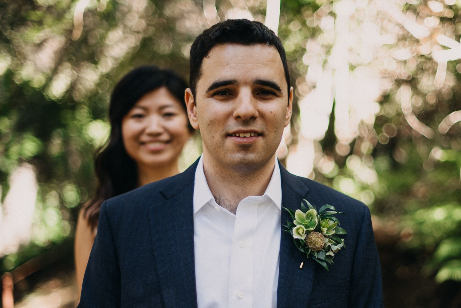 Wedding party members share joyful moments together in an outdoor garden setting with natural greenery.