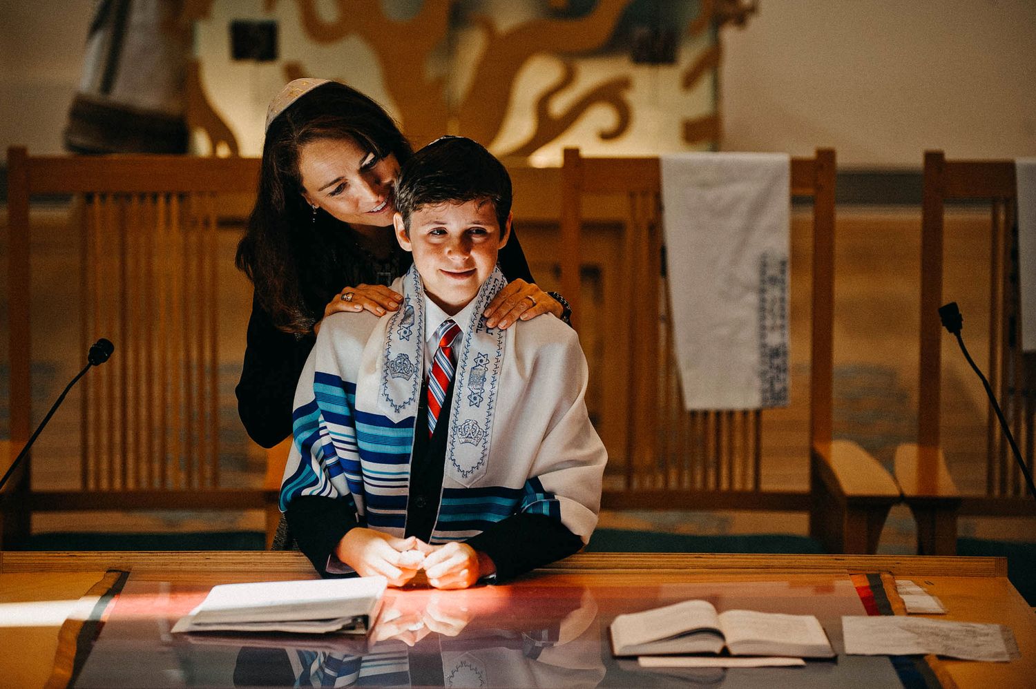 Study session between student and tutor working together at wooden desk with books and papers in warm lighting.