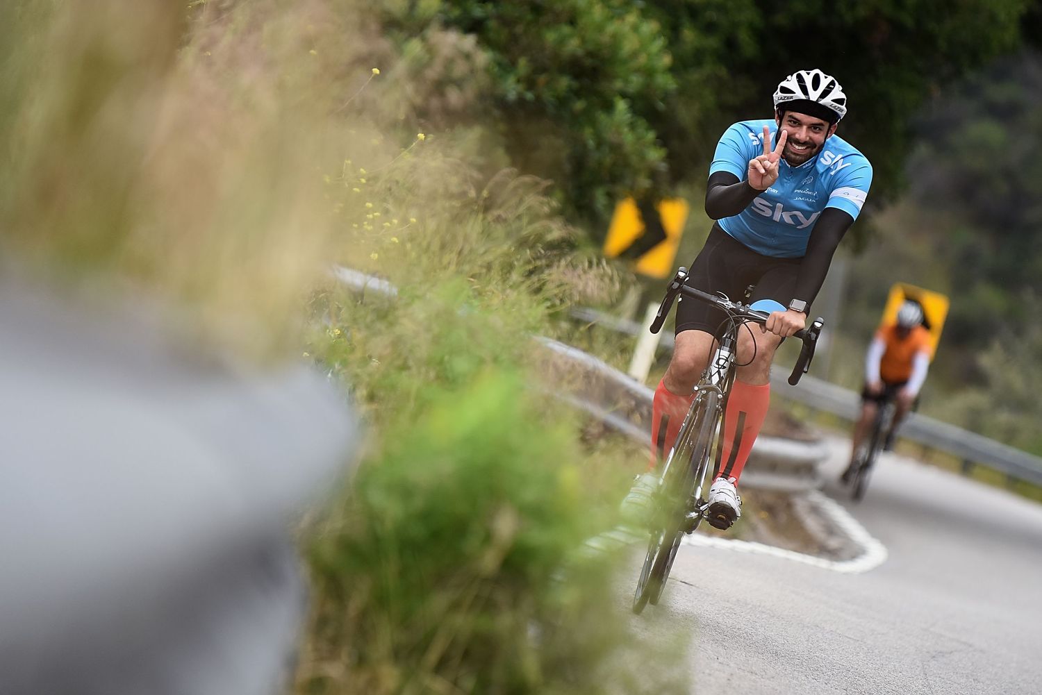 Cyclist in blue jersey leads competitors while racing on a winding road during a cycling competition.