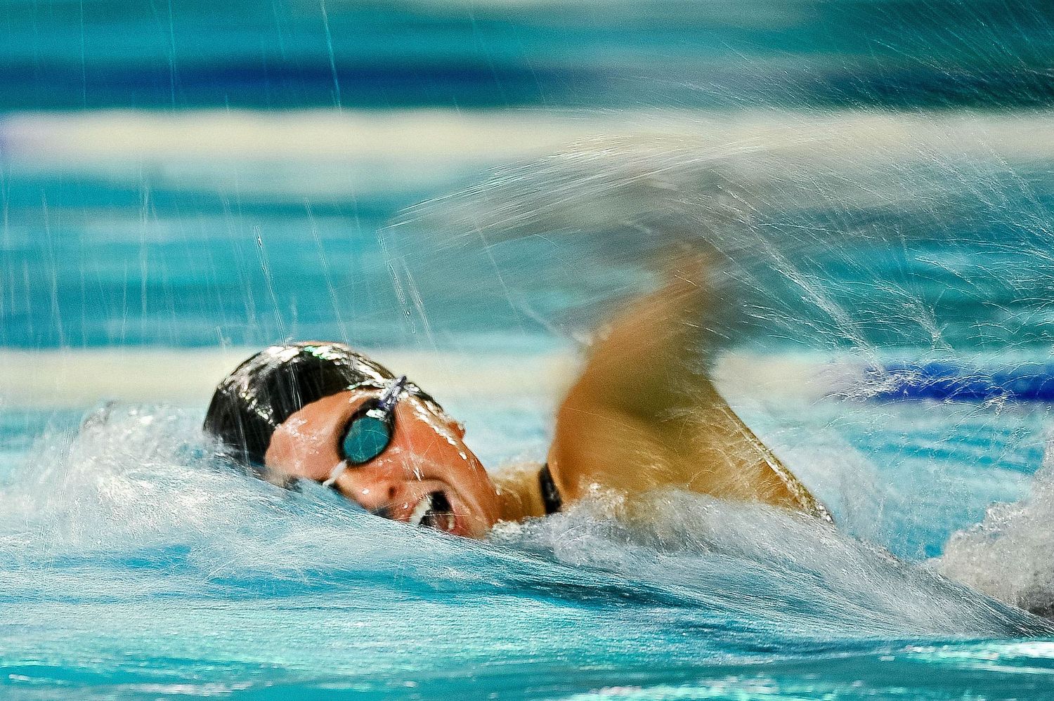 A competitive swimmer performs freestyle stroke in a pool wearing goggles and swim cap during race.