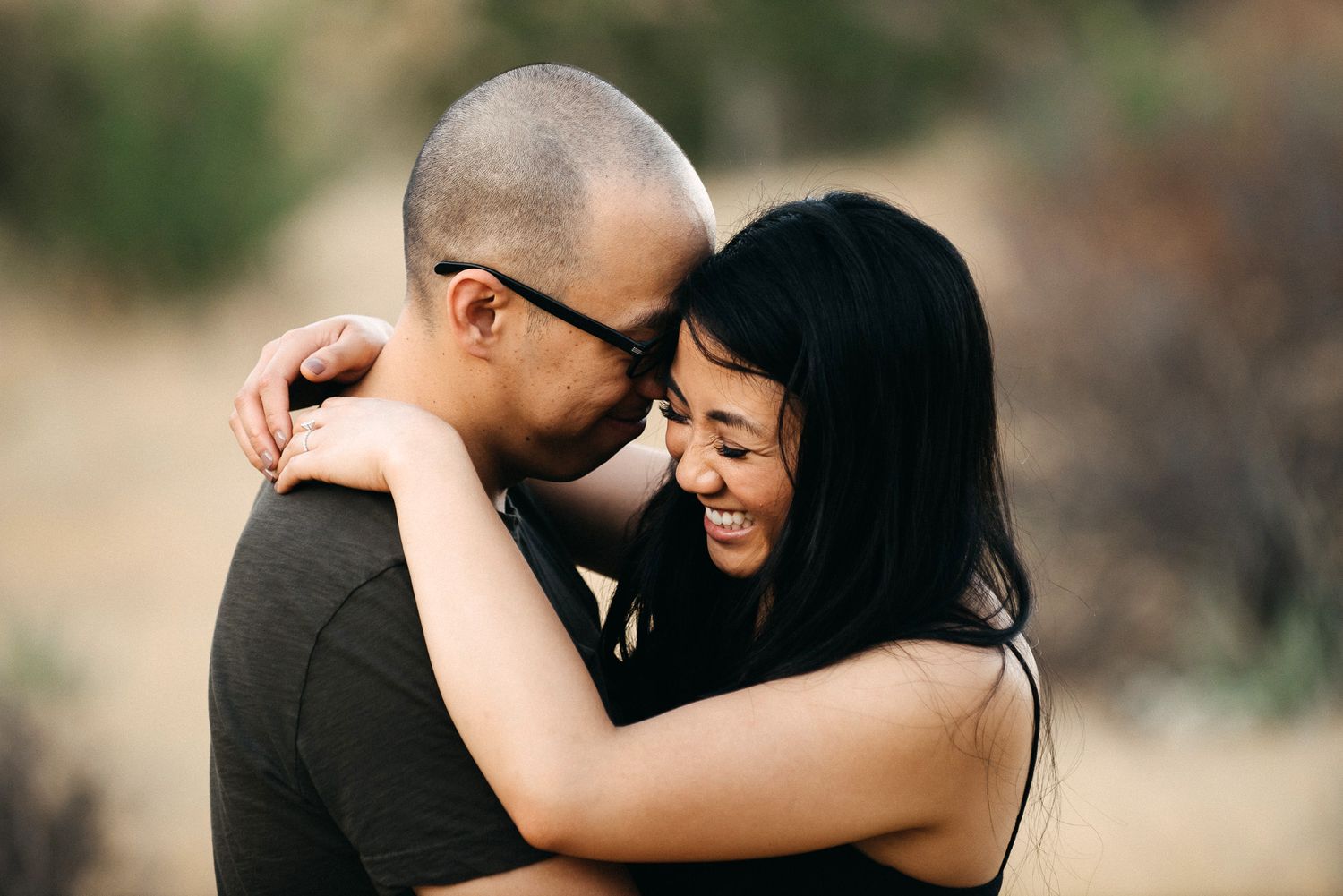 Intimate couple sharing a joyful embrace and laughter while dressed in black against a soft blurred background.