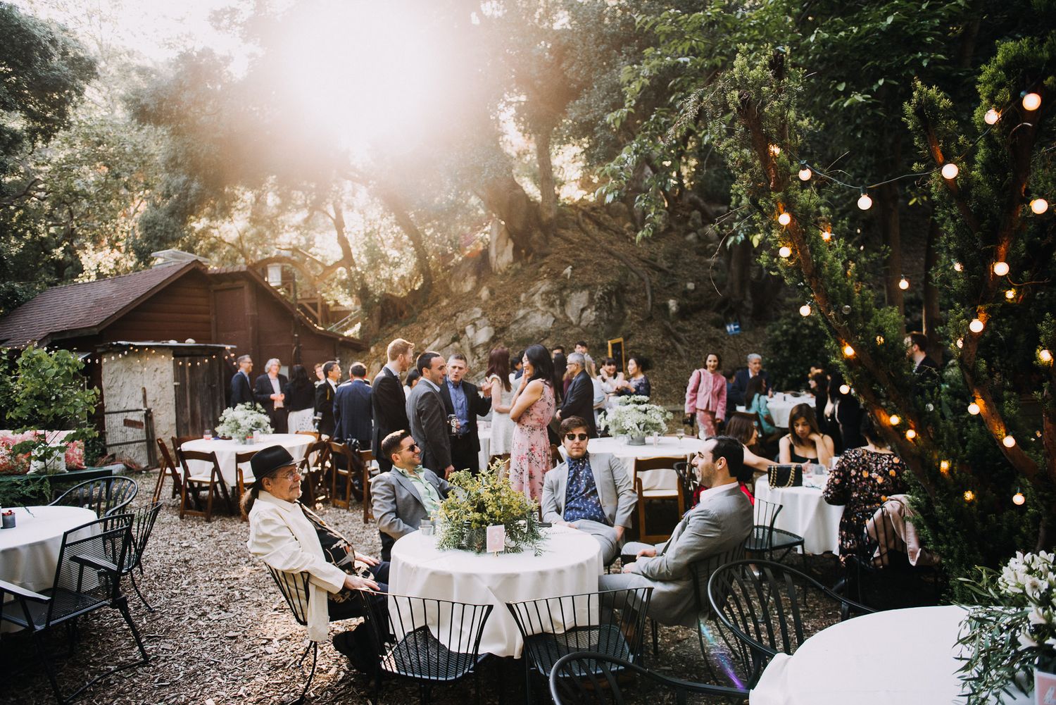 Garden wedding reception setup with round tables and string lights creating a romantic atmosphere at dusk.