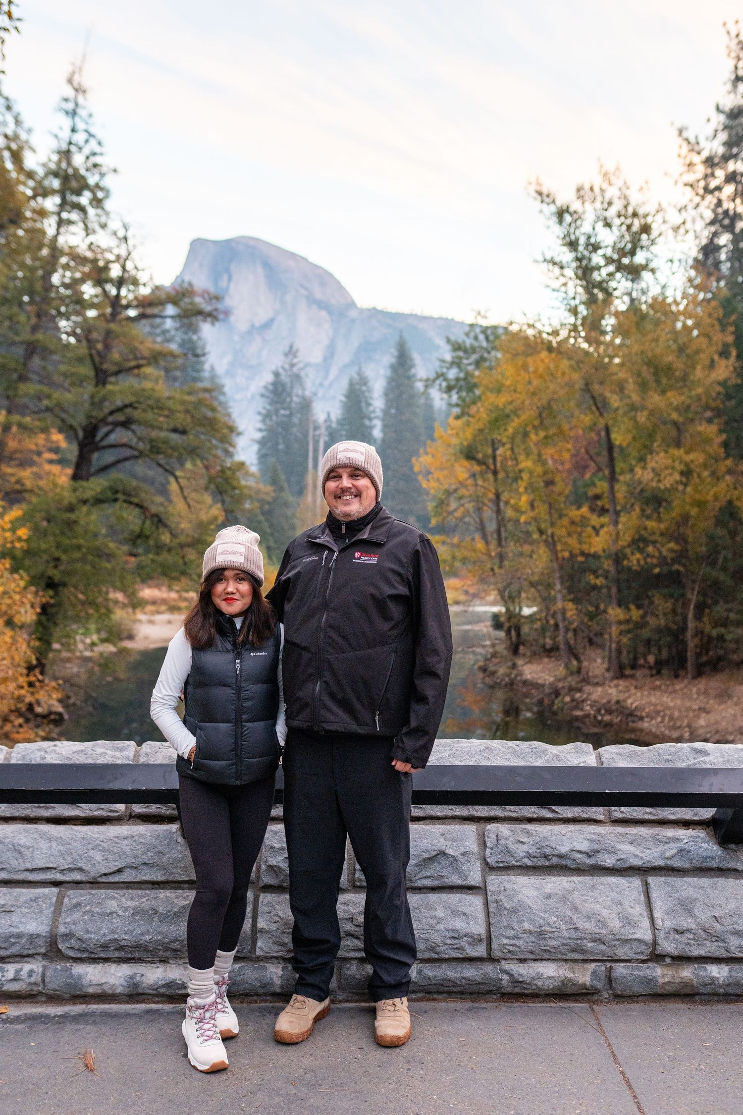 Two people sitting on a stone wall with Half Dome visible in Yosemite National Park.