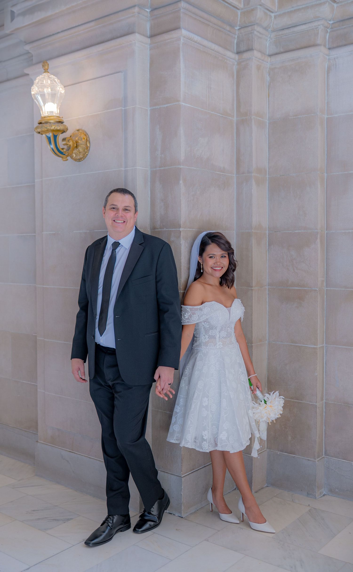 Couple in formal attire poses playfully against stone wall in series of candid wedding photos.