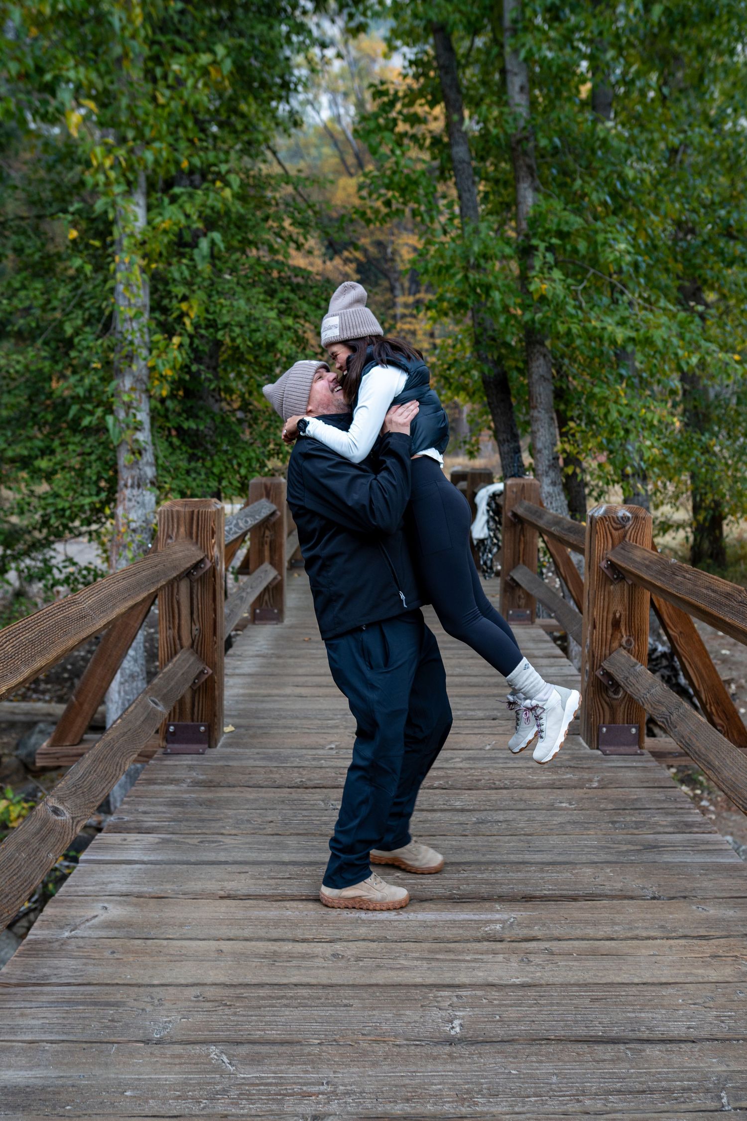 A romantic moment captured on a wooden bridge surrounded by autumn foliage.