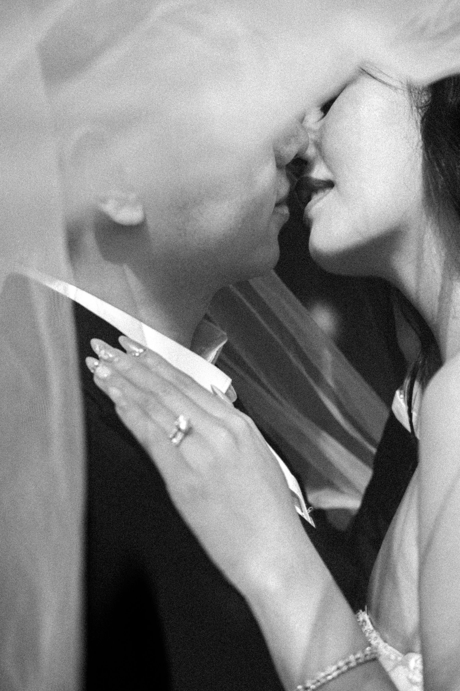 Black and white wedding photo of bride and groom kissing, bride wearing ring and veil.