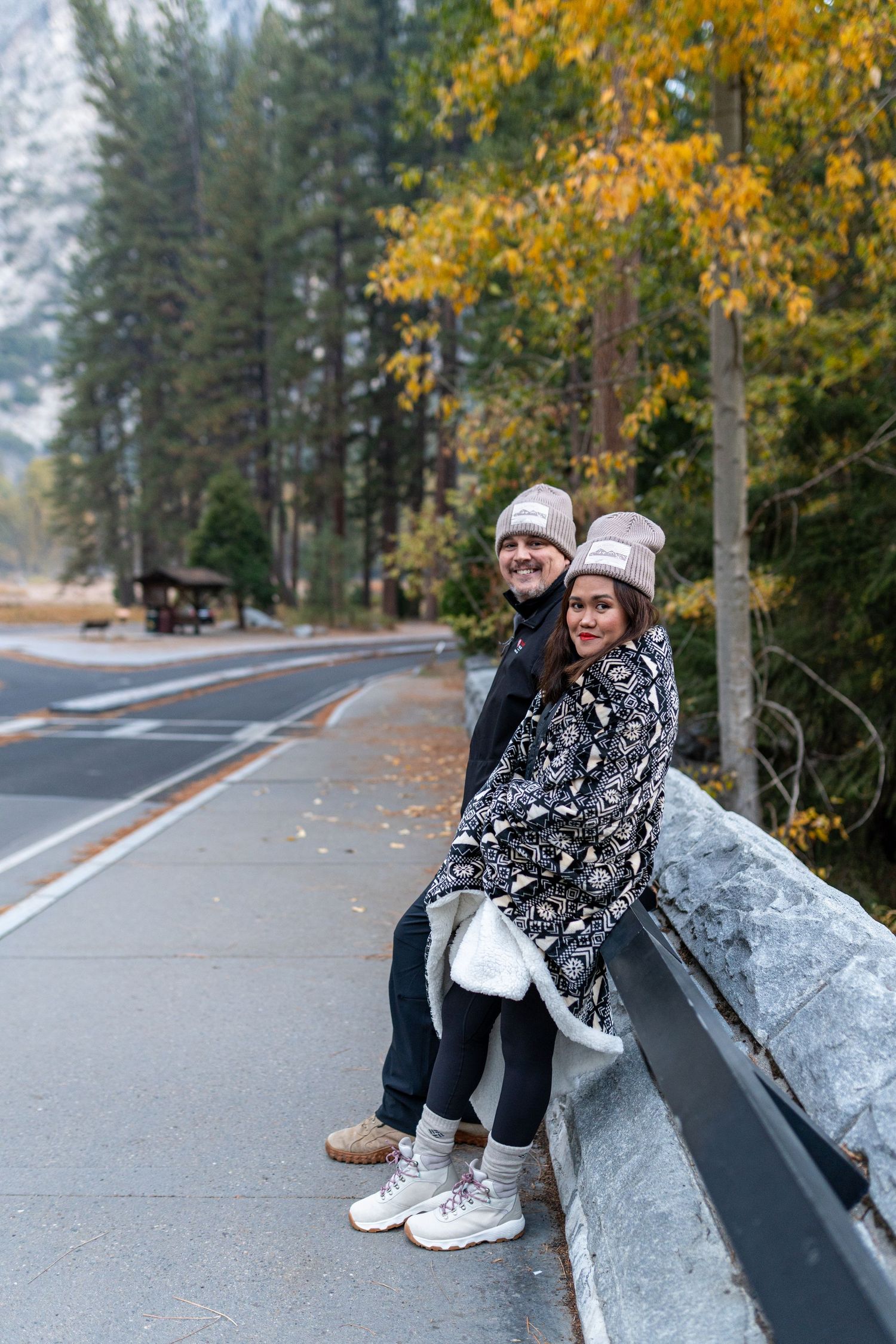People relaxing on stone barriers along a scenic mountain road in autumn.