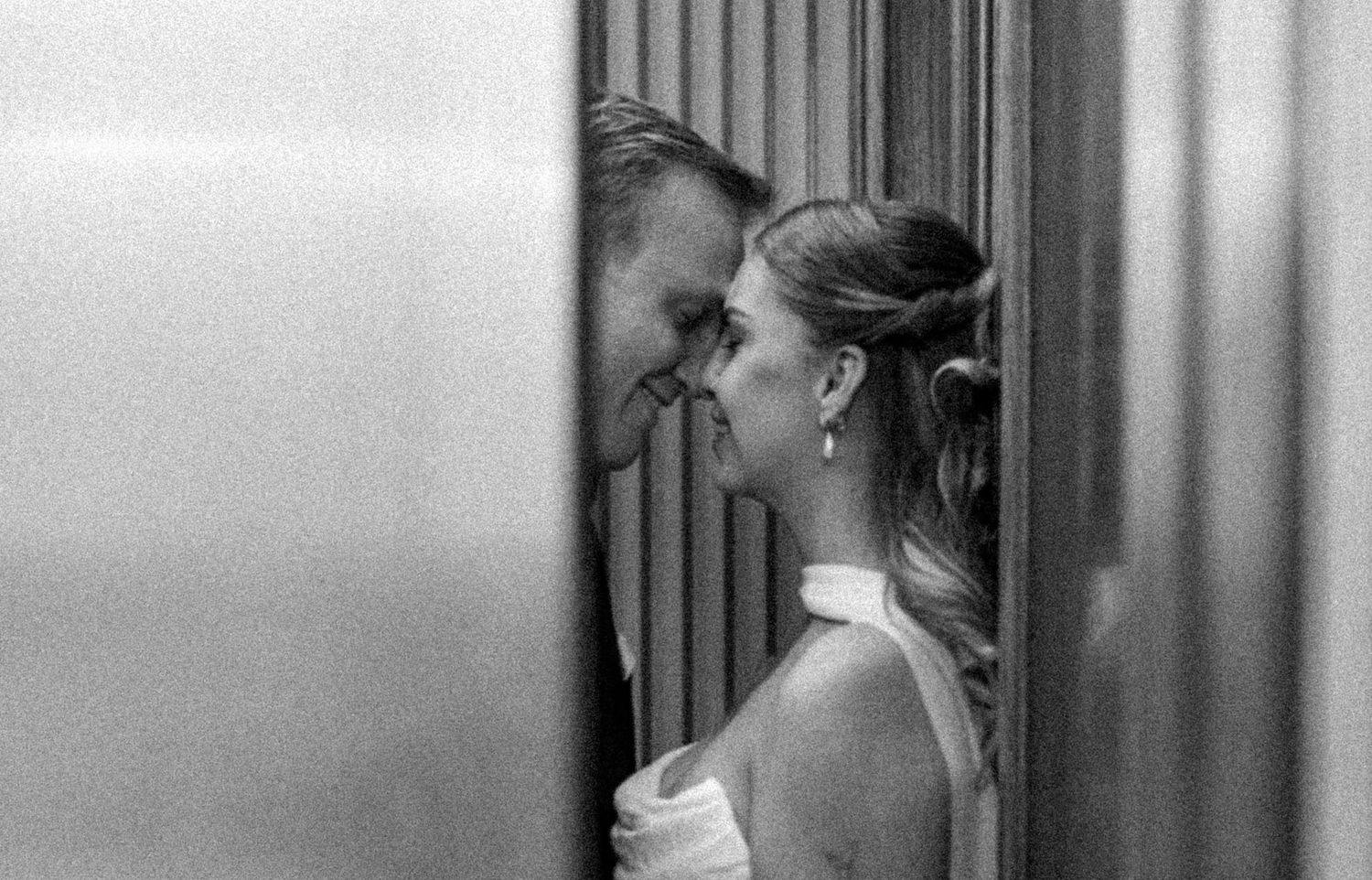Black and white photo of a bride and groom sharing an intimate moment in a narrow doorway on their wedding day.