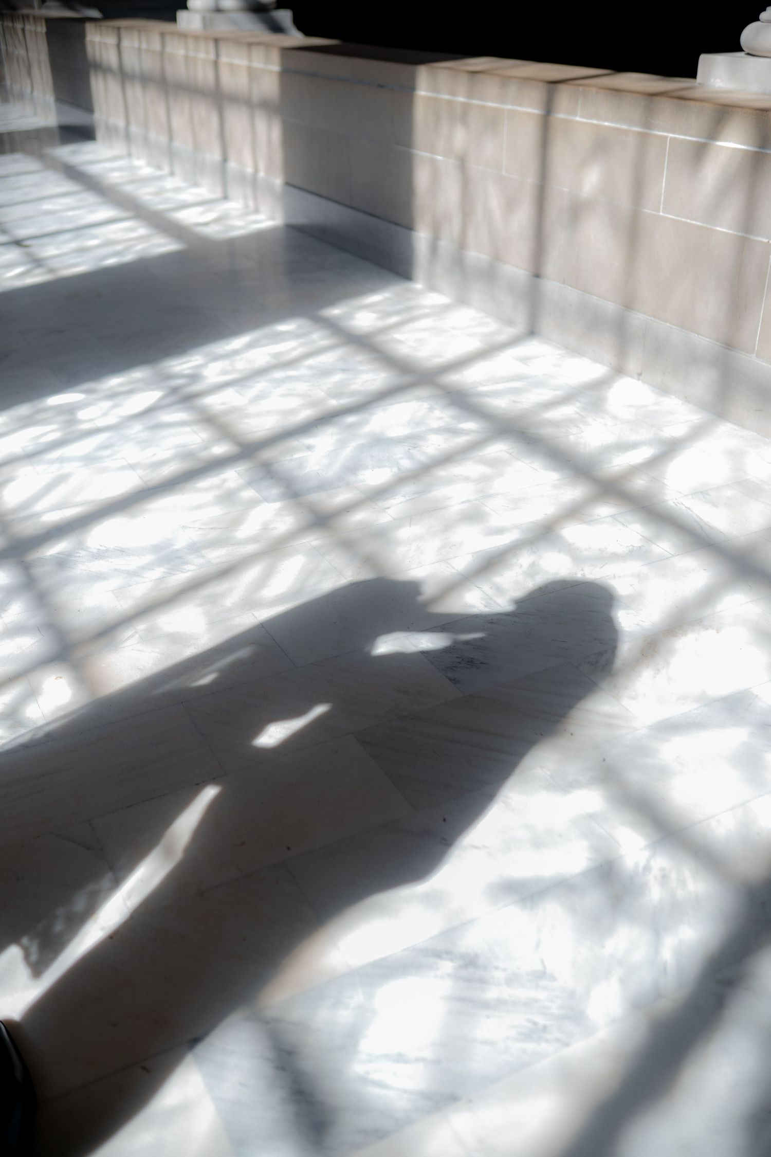 Dramatic shadows from window light create geometric patterns across a white floor in a minimalist interior space.