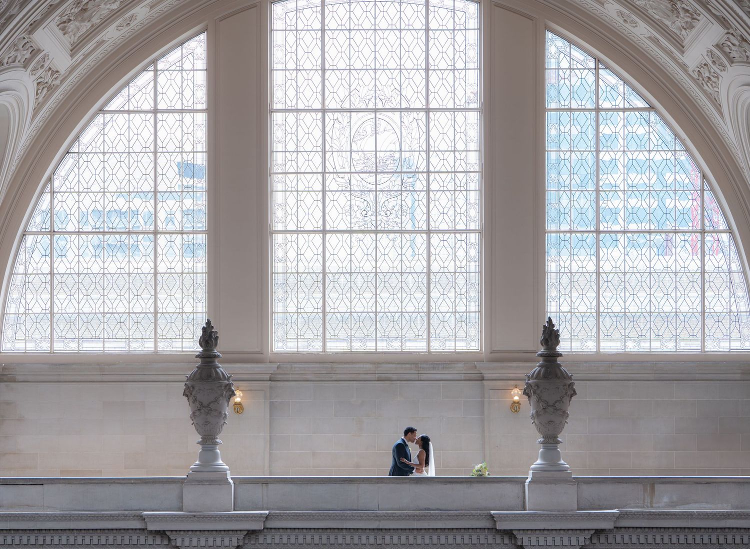 Elegant arched window with ornate white busts frames a silhouette against bright natural light in a grand architectural space.