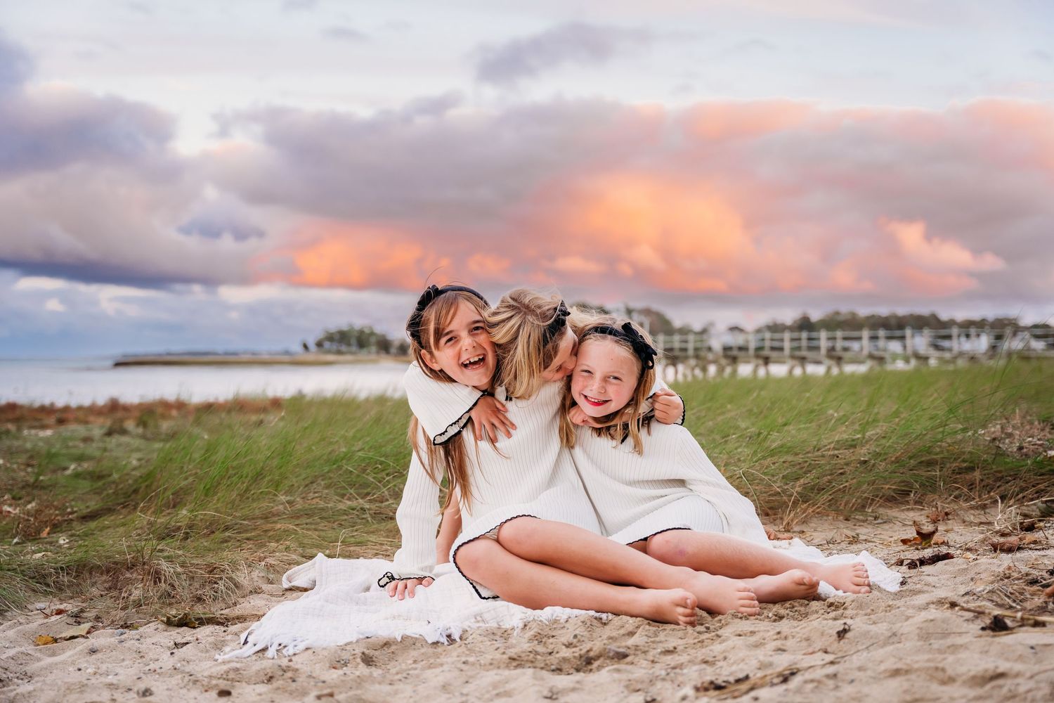 Children playing and laughing together on a beach at sunset with pink clouds in the background.