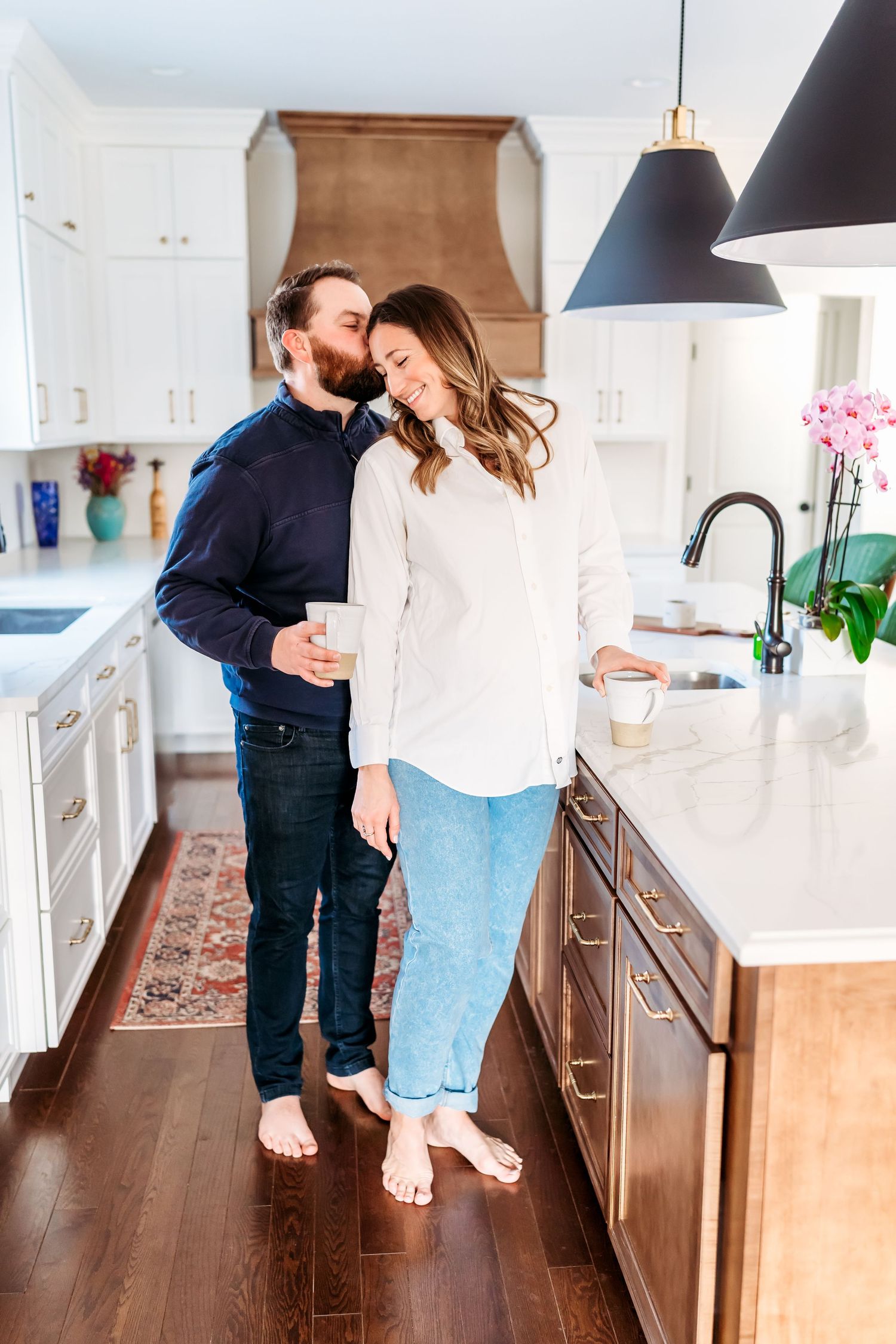 A couple dances together in a bright modern kitchen with white cabinets and pendant lights.