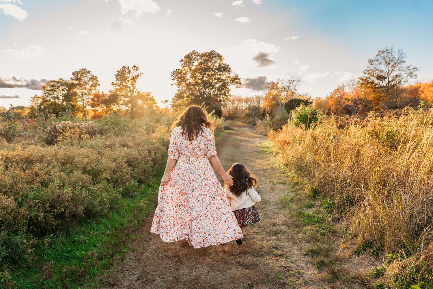 A couple in a floral dress walks through a golden field at sunset, creating a romantic silhouette against the sky.