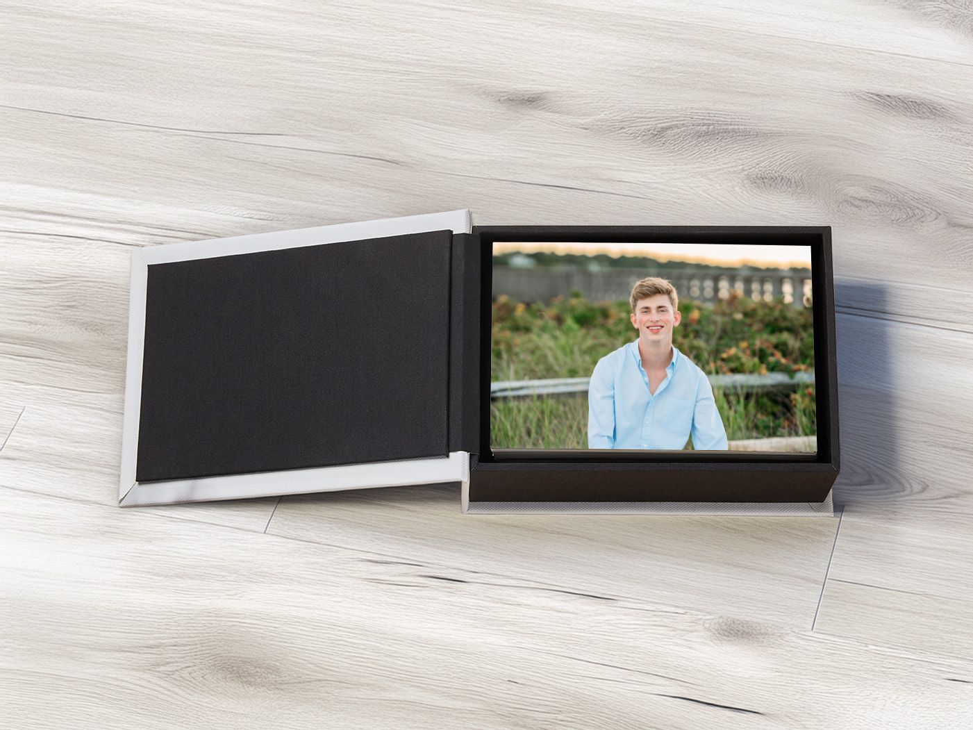 Open photo book box displaying a portrait of a smiling young man in a blue shirt on a wooden surface.