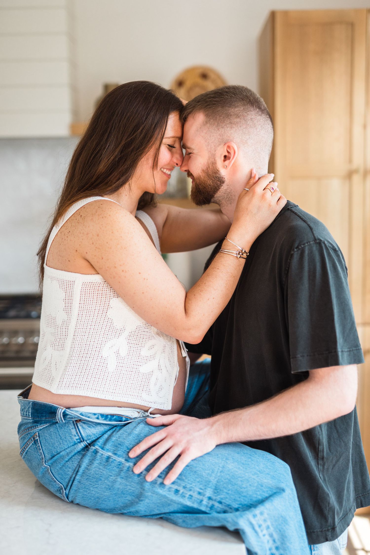 Romantic couple sharing an intimate moment while sitting on a kitchen counter in casual attire.