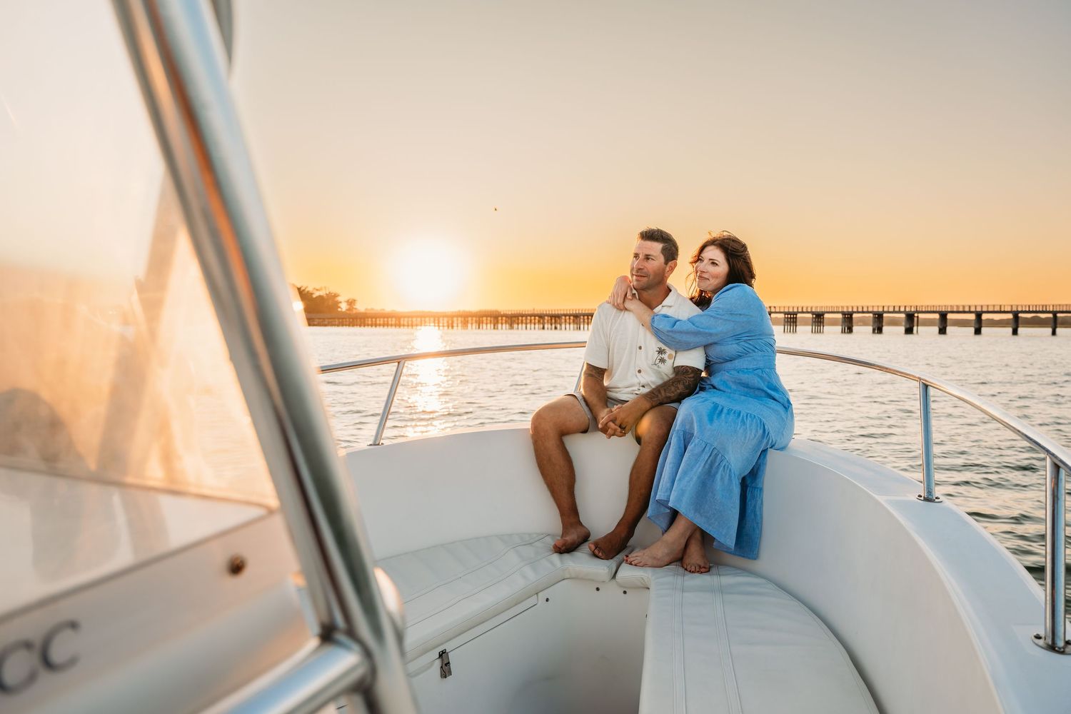 Couple in blue outfits enjoying sunset views from a luxurious yacht deck with coastal scenery in the background.