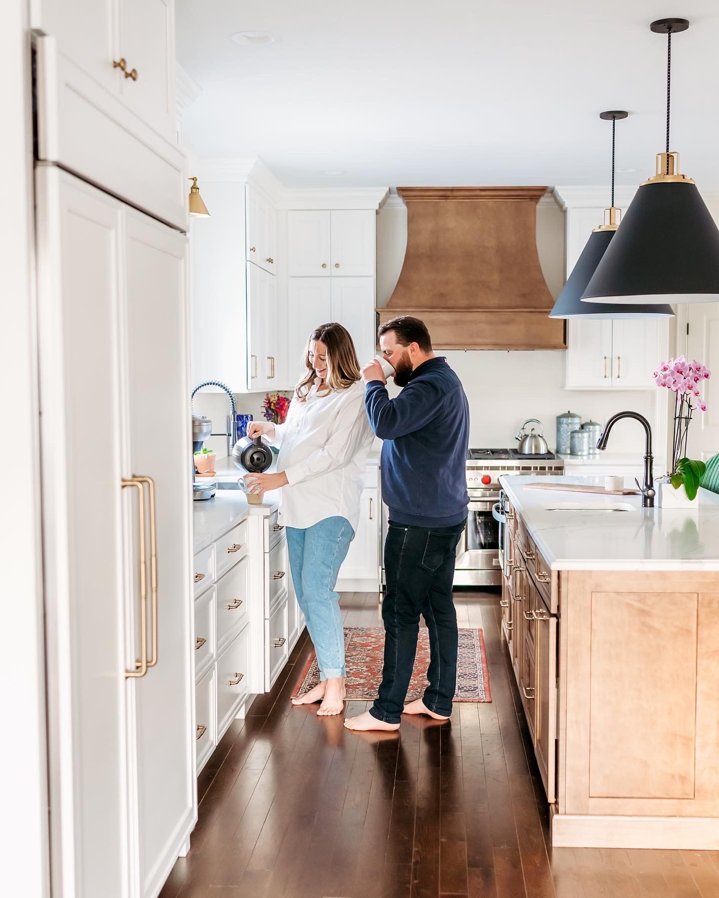 People cooking together in a bright modern white kitchen with dark wood floors and pendant lighting.