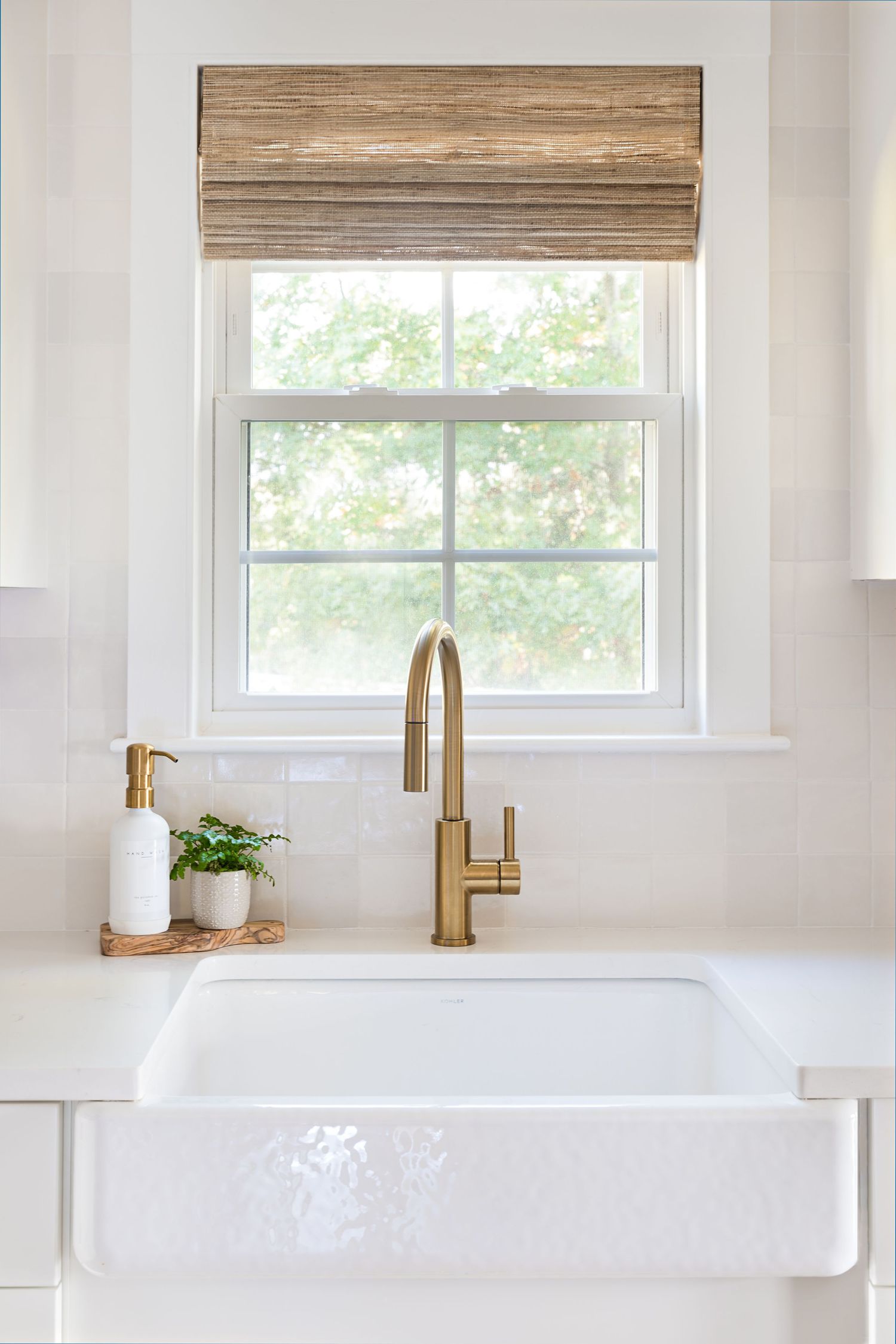 Modern farmhouse bathroom features white walls, bamboo shades, and brass fixtures with a clean, minimalist design.