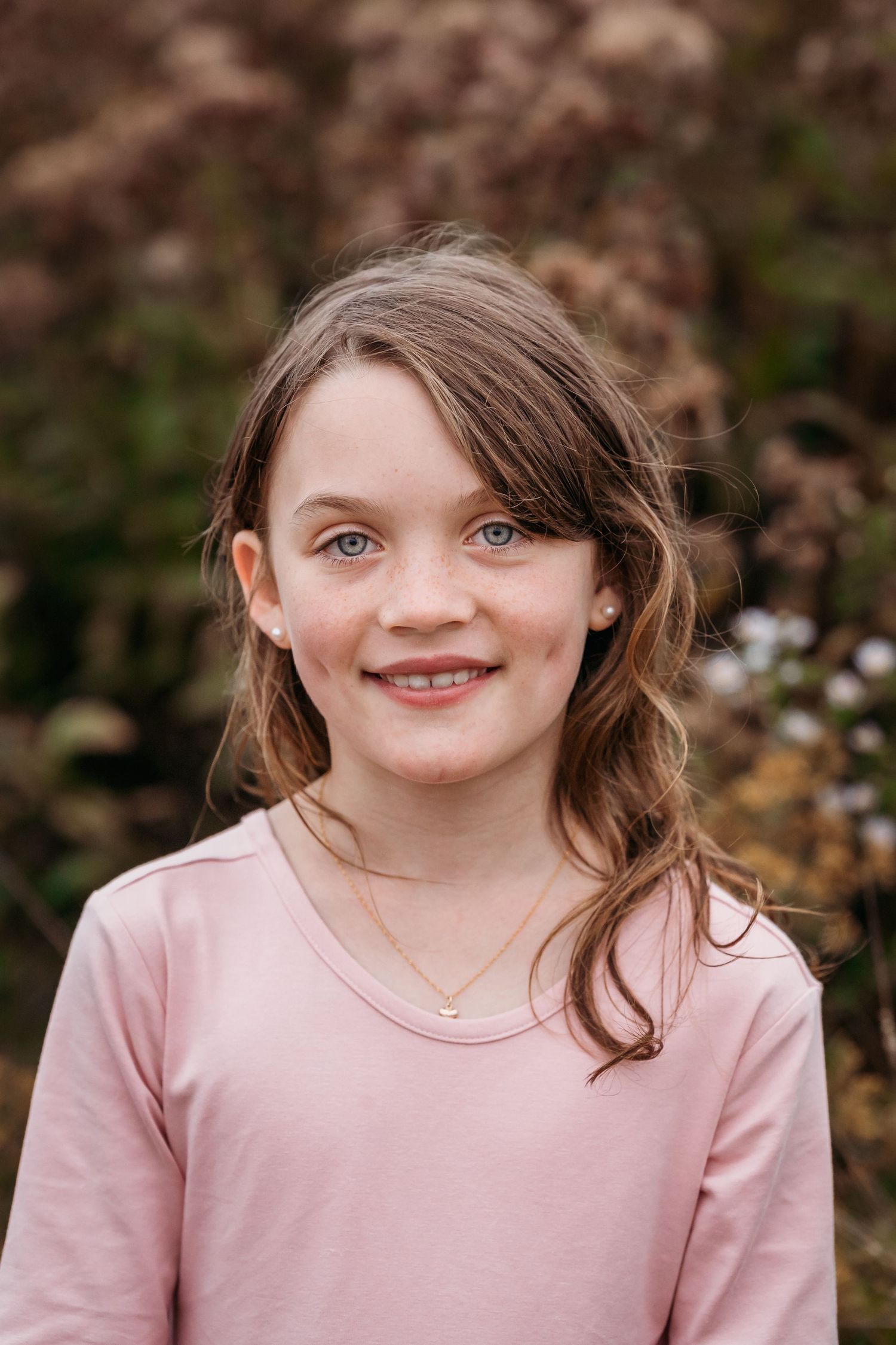 A series of five photos showing a child in a pink sweater making playful facial expressions outdoors.