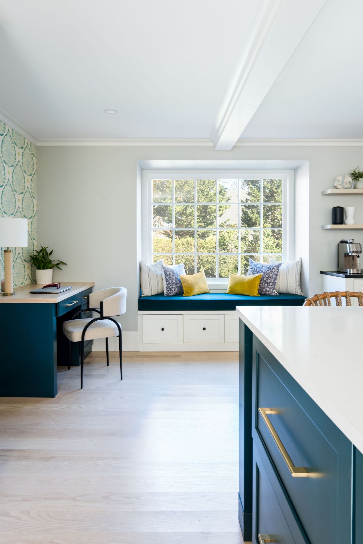 Modern white kitchen with navy blue cabinets, built-in window seat, and hardwood floors in bright sunlit space.