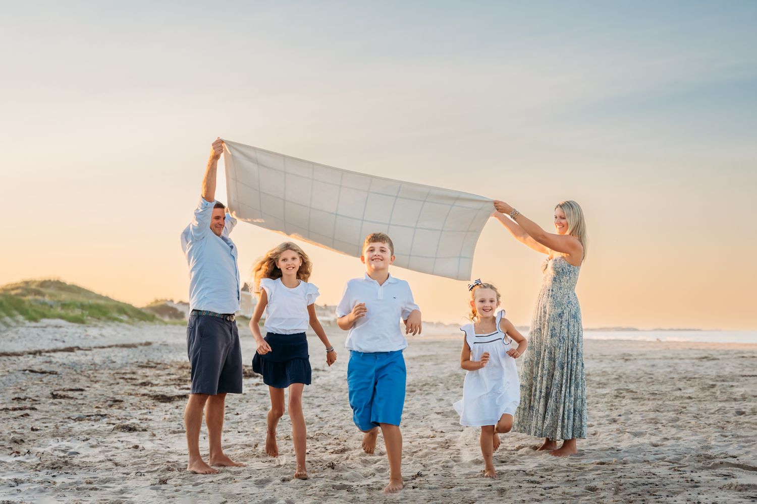 A cheerful group enjoys a sunset beach moment together while holding up a white blanket on the sandy shore.