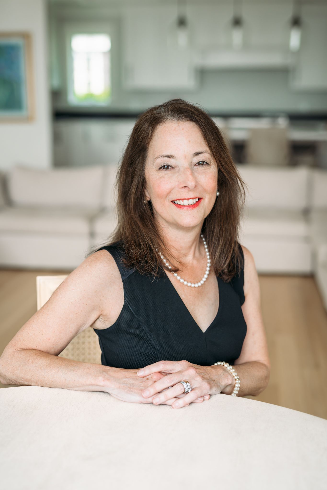 Professional headshot series showing someone in a black top and pearl necklace against a bright modern office background.