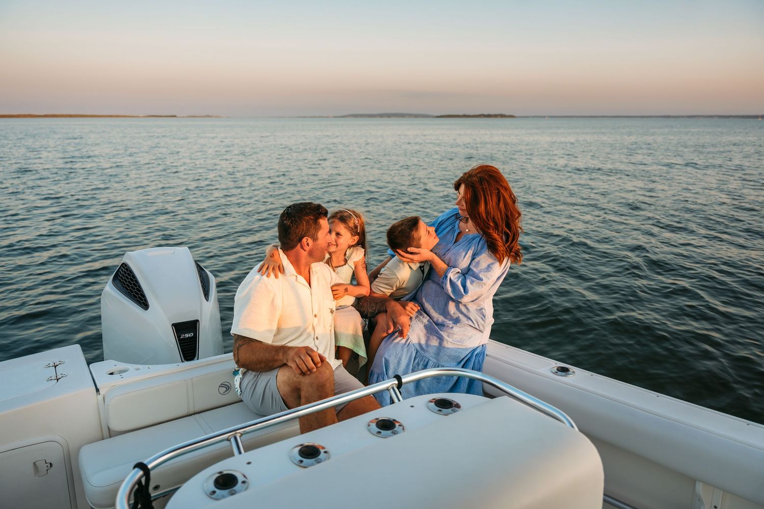 Group of people enjoying sunset drinks and conversation on a boat deck overlooking calm ocean waters.