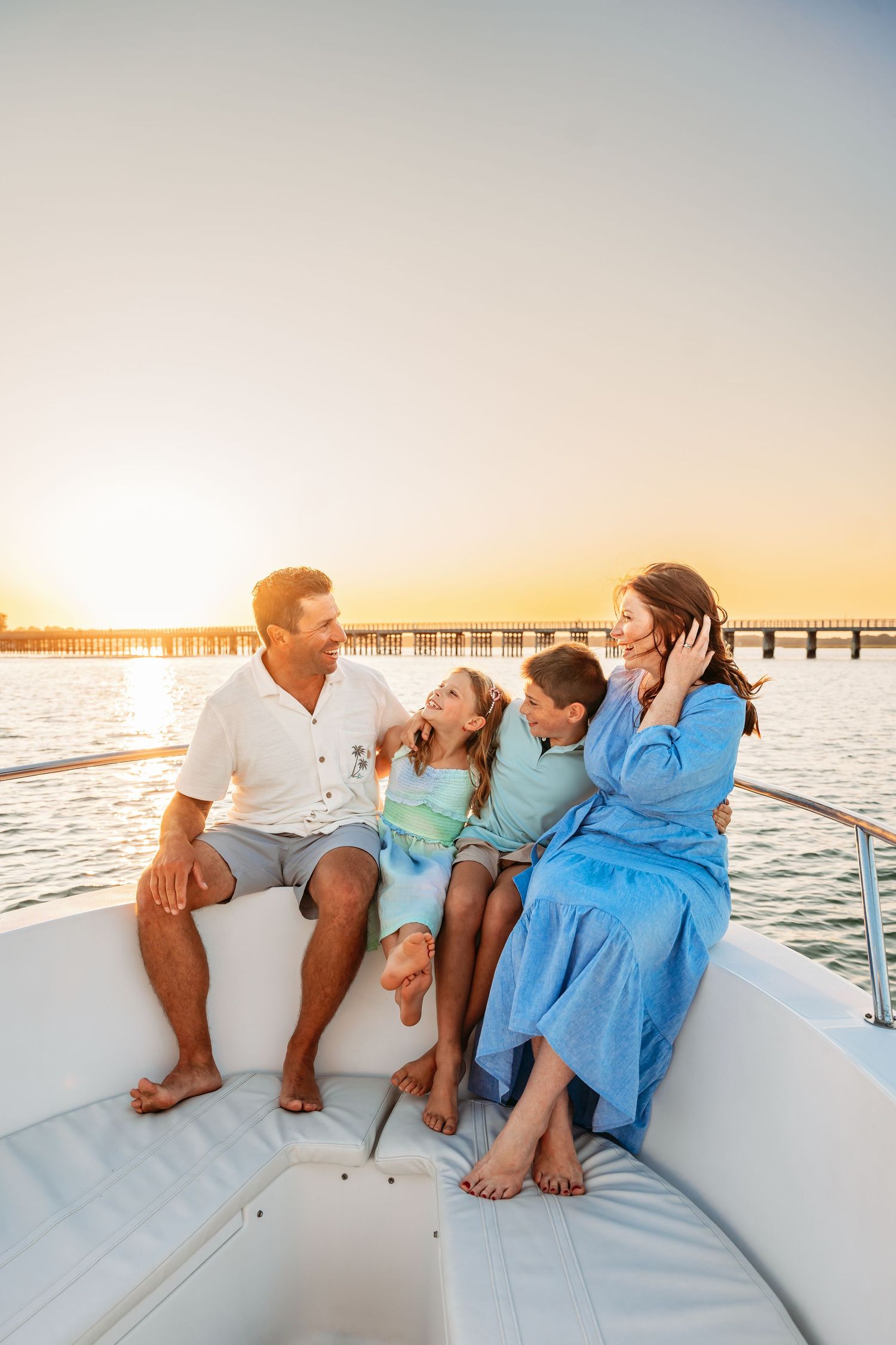 A family in coordinating blue and white outfits shares joyful moments together on a boat at sunset by the pier.