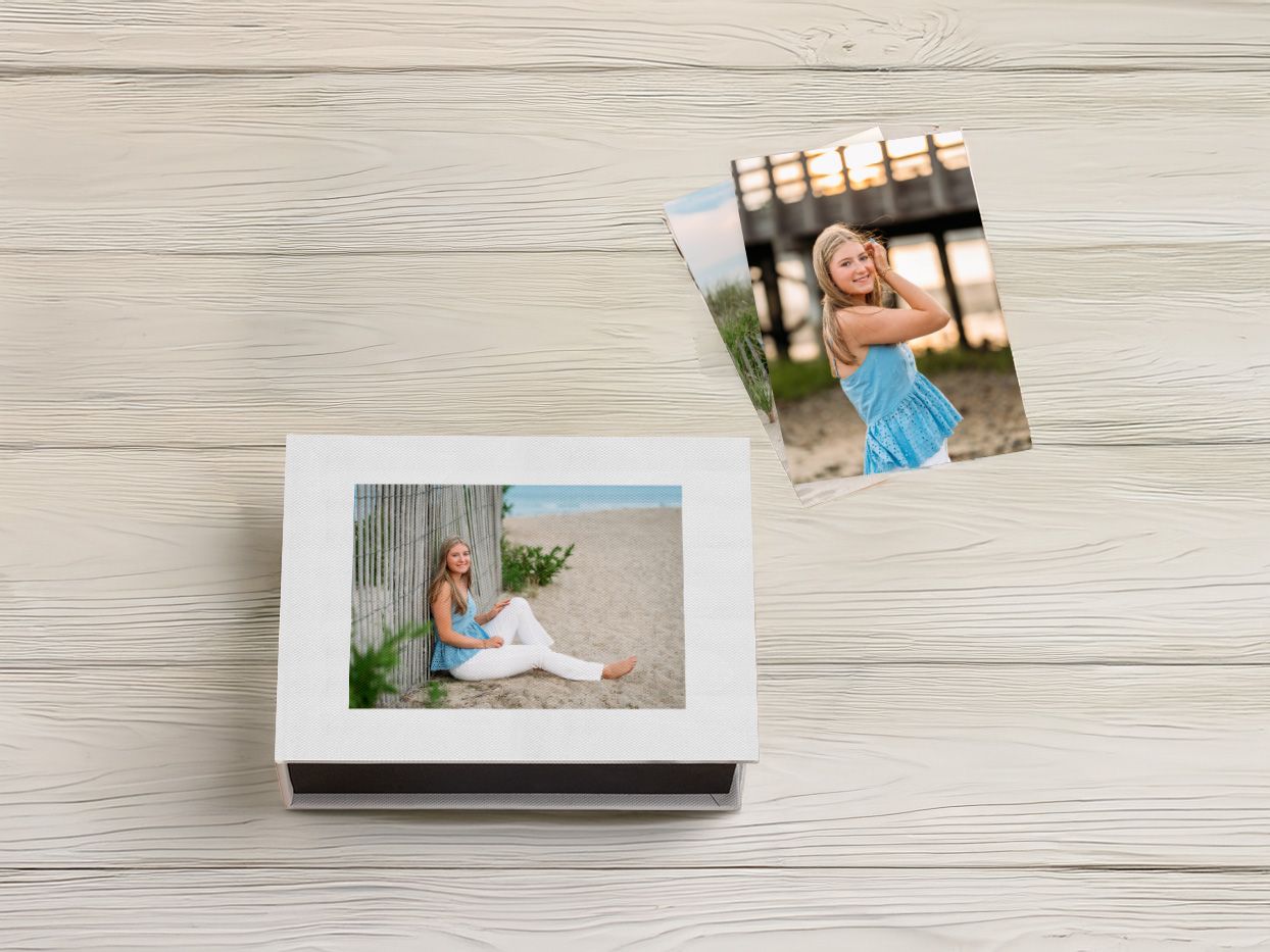 White keepsake box with senior portrait photos of a young woman in a blue dress on a beach.