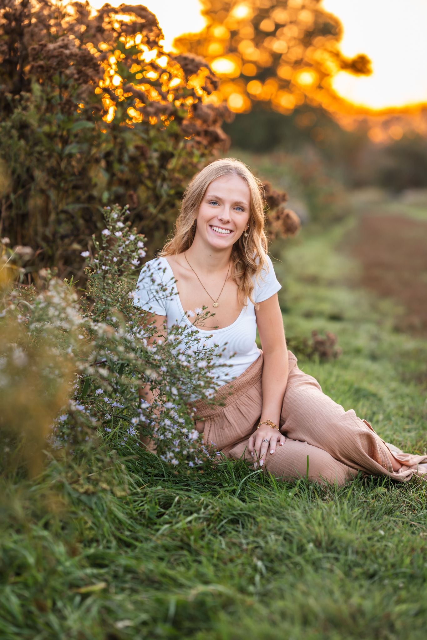 A sunset photoshoot in a grassy field with wildflowers and warm golden lighting creates a dreamy outdoor scene.