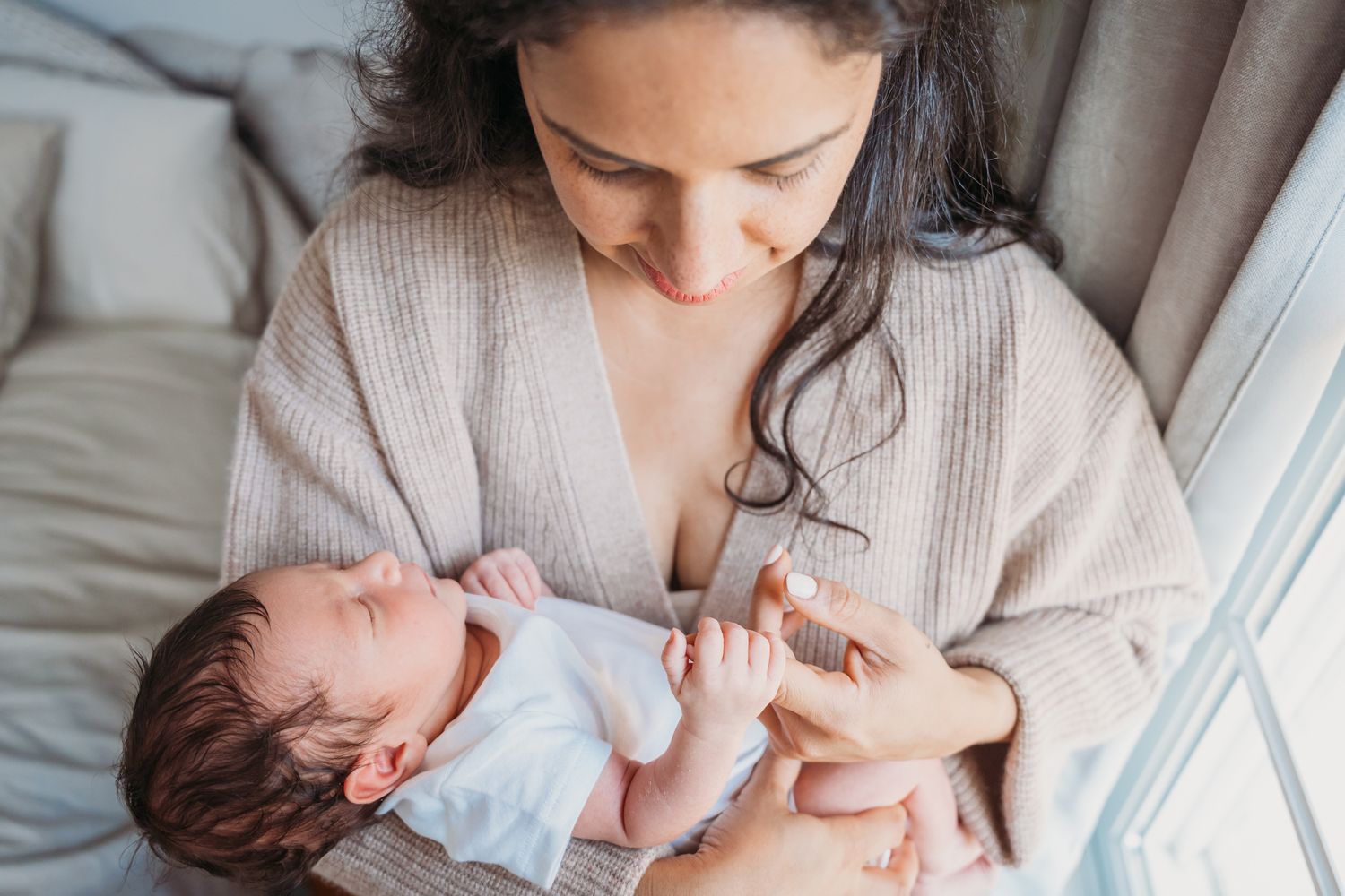 A tender moment as a mother in a beige cardigan cradles and comforts her sleeping newborn baby.