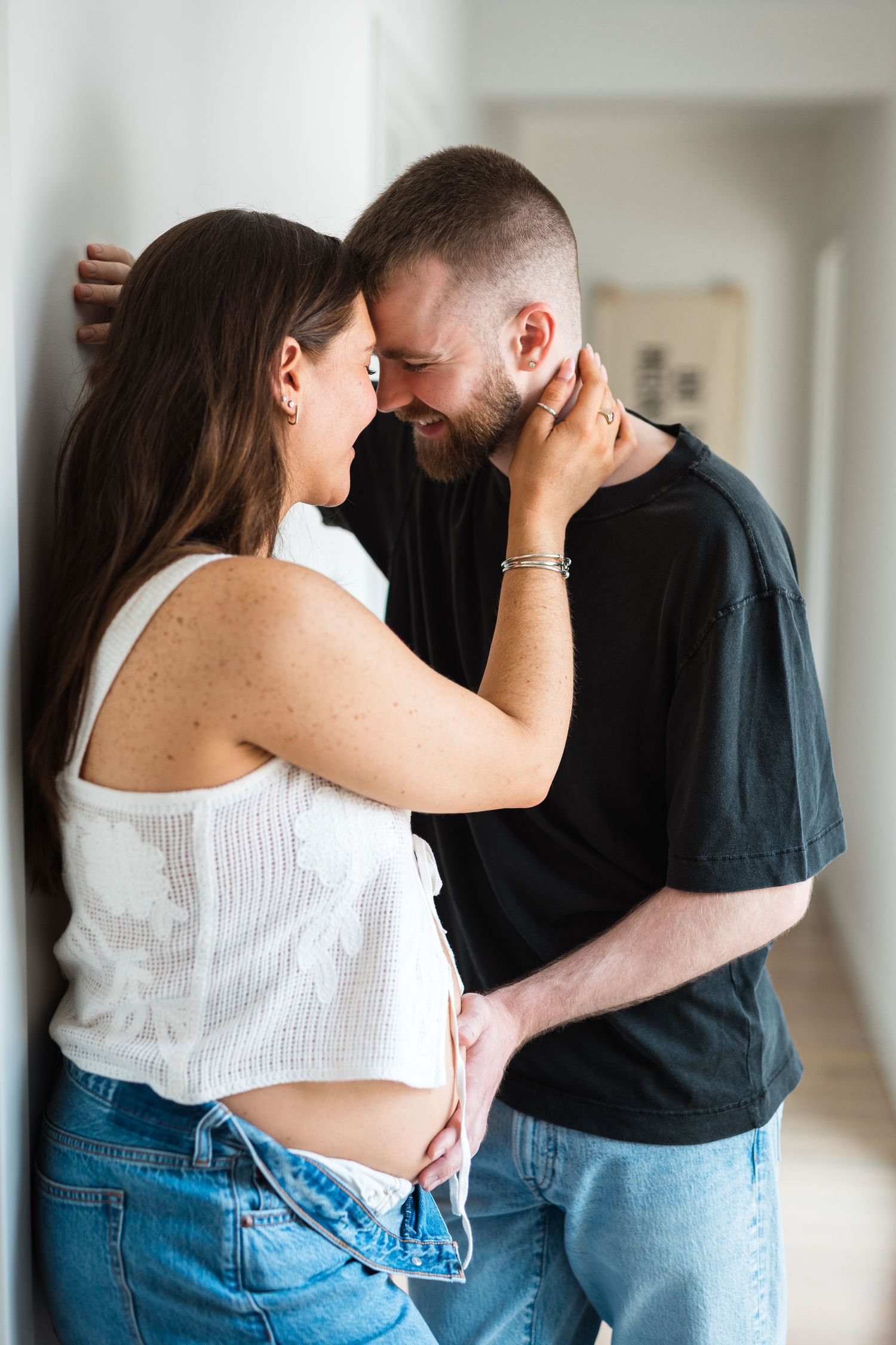 A couple in jeans and casual wear embrace and dance together in a bright indoor space.